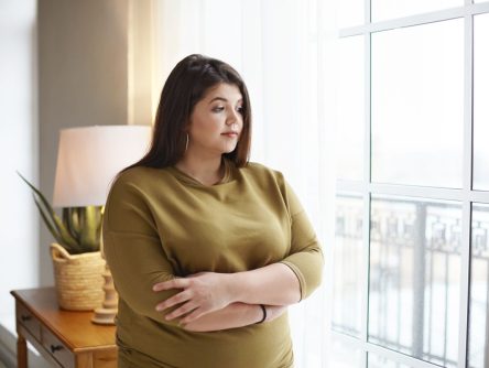 People, lifestyle and body positivity concept. Beautiful young brunette female with extra pounds standing by window at home, crossing arms on her chest, having thoughtful pensive look, pondering